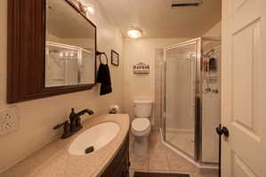 2nd Bathroom featuring a shower stall, vanity, light tile patterned floors, a textured ceiling, and a textured wall