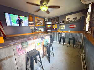 Indoor dry bar with unfinished concrete floors, ceiling fan, and wood counters