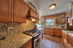 Kitchen featuring Gas stove/oven with hood, stone tile floors, Granite countertops, and glass fronted cabinets