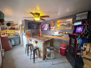 Indoor dry bar with unfinished concrete floors and ceiling fan