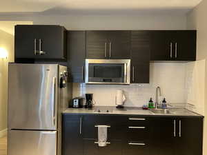 Kitchen with stainless steel appliances, dark cabinetry. Appliances include: free standing fridge, oven/microwave combo, cooktop, and small kitchen appliances.