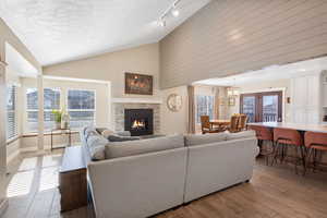 Living room with light wood-style floors, a stone fireplace, a high textured ceiling, french doors, and track lighting