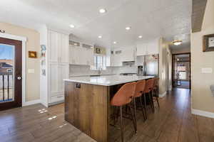 Two tone kitchen with dark wood finished floors, glass insert cabinets, dual tone cabinetry, a kitchen island, and a kitchen breakfast bar