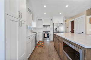 Kitchen featuring two tone cabinetry, stainless steel appliances, light stone countertops, a kitchen island, and backsplash