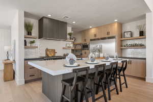 Kitchen featuring open shelves, an island with sink, built in appliances, light wood-style floors, and a kitchen breakfast bar