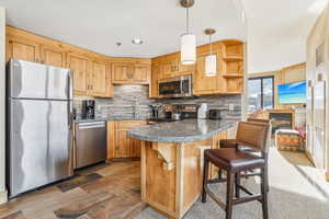 Kitchen featuring stainless steel appliances, a kitchen breakfast bar, decorative light fixtures, a peninsula, and decorative backsplash