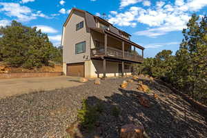 Rear view of property with a gambrel roof, concrete driveway, a garage, and stucco siding
