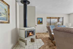 Tiled living area featuring a wood stove, a textured ceiling, and carpet