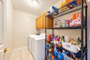 Laundry area featuring washing machine and clothes dryer, cabinet space, and light floors