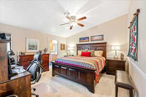 Bedroom featuring a desk, light carpet, ceiling fan, ensuite bathroom, and vaulted ceiling