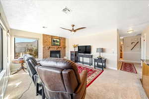 Carpeted living room featuring ceiling fan, a fireplace, and a textured ceiling