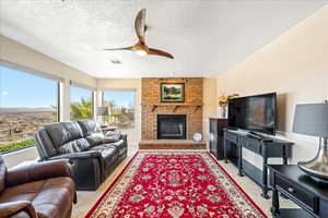 Living room with ceiling fan, a brick fireplace, light colored carpet, and a textured ceiling