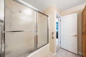 Full bath featuring enclosed tub / shower combo and light tile patterned floors