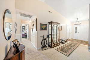 Foyer entrance featuring light carpet, vaulted ceiling, and hanging lights