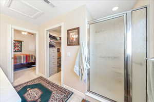 Ensuite bathroom featuring a stall shower, light colored carpet, a walk in closet, and a ceiling fan