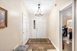 Foyer with light tile patterned floors, a textured wall, hanging lights, and a textured ceiling