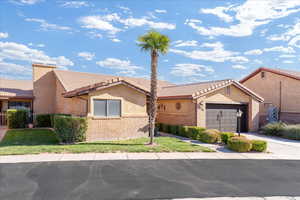 Mediterranean / spanish house with a garage, brick siding, driveway, a tiled roof, and stucco siding