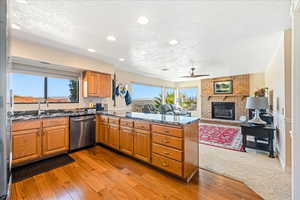 Kitchen with dark stone counters, light wood-type flooring, a ceiling fan, dishwasher, and wood finish cabinets