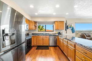 Kitchen featuring stainless steel appliances, dark stone counters, wood finish cabinetry, recessed lighting, and a textured ceiling