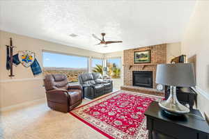 Living area featuring ceiling fan, carpet floors, a brick fireplace, and a textured ceiling