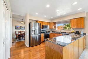 Kitchen with stainless steel appliances, dark stone counters, wood finish cabinetry, light wood-style flooring, and recessed lighting