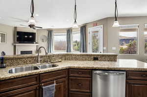 Kitchen featuring hanging light fixtures, a fireplace, stainless steel dishwasher, light stone counters, and dark wood finish cabinetry