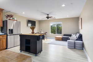 Two tone kitchen featuring stainless steel refrigerator with ice dispenser, light wood-style flooring, a ceiling fan, open floor plan, and recessed lighting