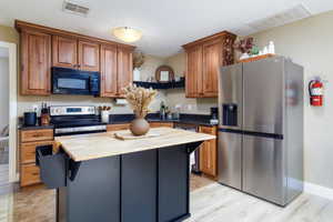 Kitchen featuring stainless steel appliances, a kitchen island, wood finish cabinets, butcher block counters, and a kitchen breakfast bar