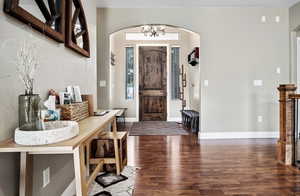 Foyer entrance with dark wood finished floors, arched walkways, and hanging lights