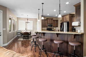 Kitchen featuring a peninsula, light stone countertops, stainless steel appliances, a kitchen bar, and dark wood-style floors