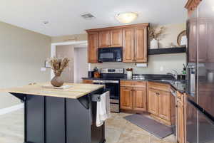 Kitchen with stainless steel appliances, wood finish cabinets, dark stone counters, a kitchen island, and light tile patterned flooring