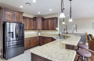 Kitchen with stainless steel refrigerator with ice dispenser, a peninsula, light stone counters, hanging light fixtures, and a kitchen bar