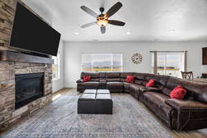 Living area featuring wood finished floors, a stone fireplace, a ceiling fan, and a textured ceiling