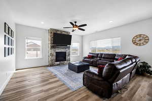 Living area with a stone fireplace, light wood-style flooring, ceiling fan, and recessed lighting