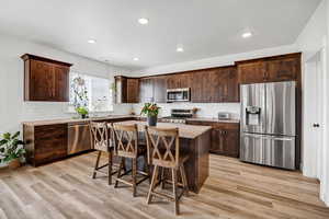 Kitchen featuring dark wood finish cabinetry, stainless steel appliances, a breakfast bar area, a center island, and recessed lighting