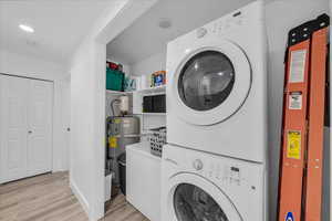 Laundry area featuring water heater, light wood-style floors, stacked washer and clothes dryer, and recessed lighting