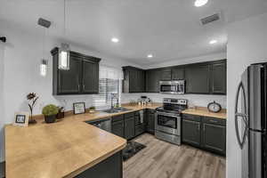 Kitchen featuring stainless steel appliances, pendant lighting, light countertops, and a peninsula