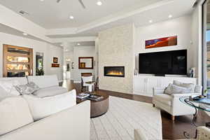 Living area with wood finished floors, a fireplace, a ceiling fan, recessed lighting, and a tray ceiling