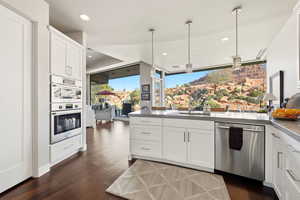 Kitchen with white cabinetry, decorative light fixtures, stainless steel appliances, dark wood-style floors, and a peninsula