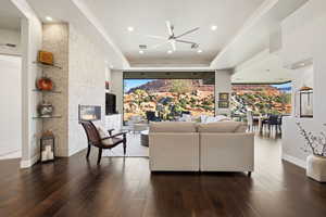 Living room with a raised ceiling, dark wood-style floors, ceiling fan, a fireplace, and recessed lighting