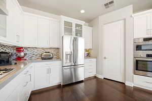 Kitchen with glass insert cabinets, stainless steel appliances, white cabinetry, dark wood-type flooring, and recessed lighting