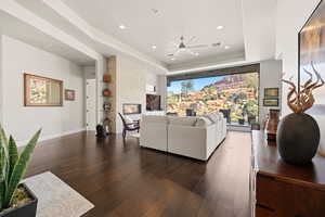 Living area with a tray ceiling, a ceiling fan, dark wood finished floors, a large fireplace, and recessed lighting