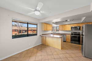 Kitchen with stainless steel appliances, a tray ceiling, a ceiling fan, a peninsula, and light tile patterned flooring