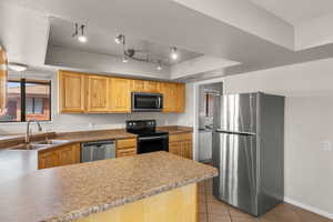 Kitchen featuring a tray ceiling, stainless steel appliances, light tile patterned flooring, light wood finish cabinets, and rail lighting