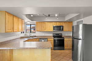 Kitchen with stainless steel appliances, a tray ceiling, a peninsula, and light tile patterned floors