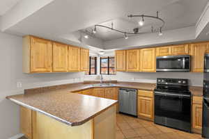 Kitchen featuring black appliances, a raised ceiling, a peninsula, light tile patterned flooring, and dark countertops