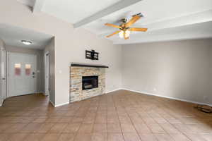 Unfurnished living room with a ceiling fan, a fireplace, beamed ceiling, and light tile patterned floors