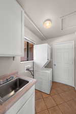 Laundry area with light tile patterned floors, stacked washer / dryer, and cabinet space