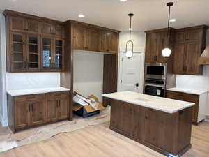 Kitchen featuring glass insert cabinets, stainless steel appliances, a center island, pendant lighting, and light stone countertops