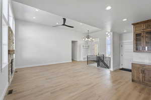 Unfurnished living room with ceiling fan, light wood-type flooring, a chandelier, and a stone fireplace
